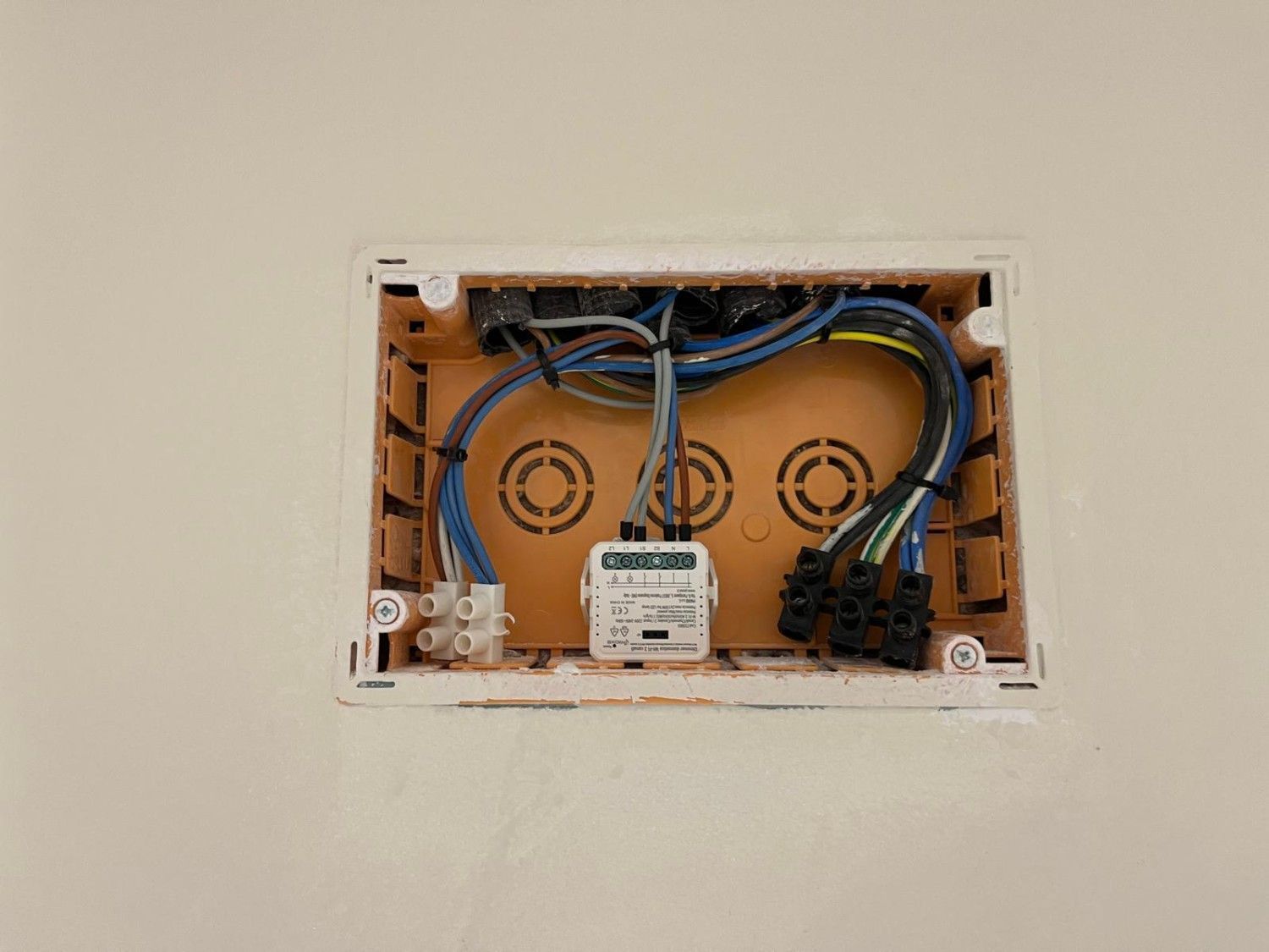 Caja de conexiones eléctricas abierta con cables azules y negros montada en una abertura de la pared.