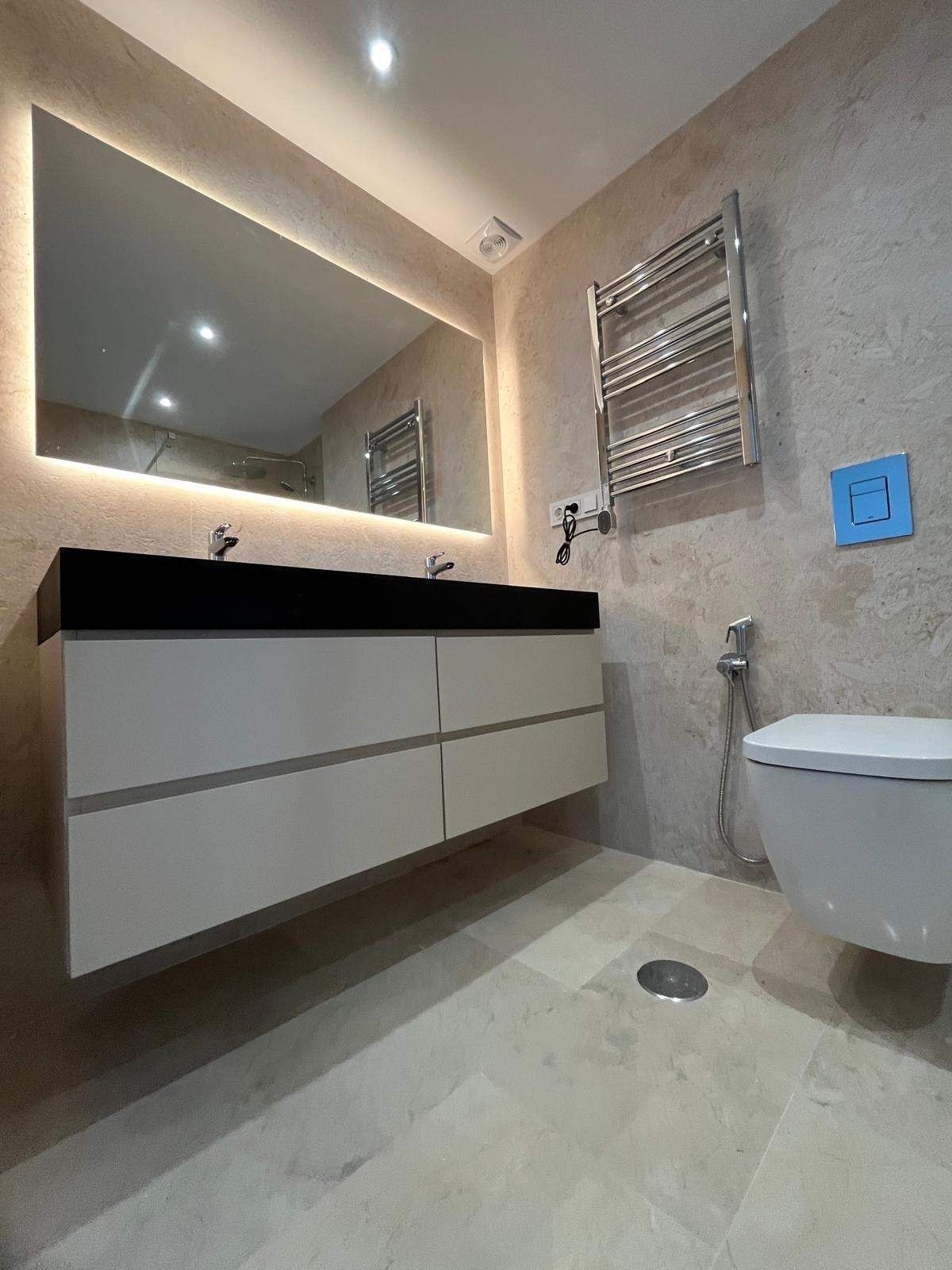 Baño moderno con lavabo suspendido, espejo grande, toallero eléctrico de pared e inodoro suspendido.