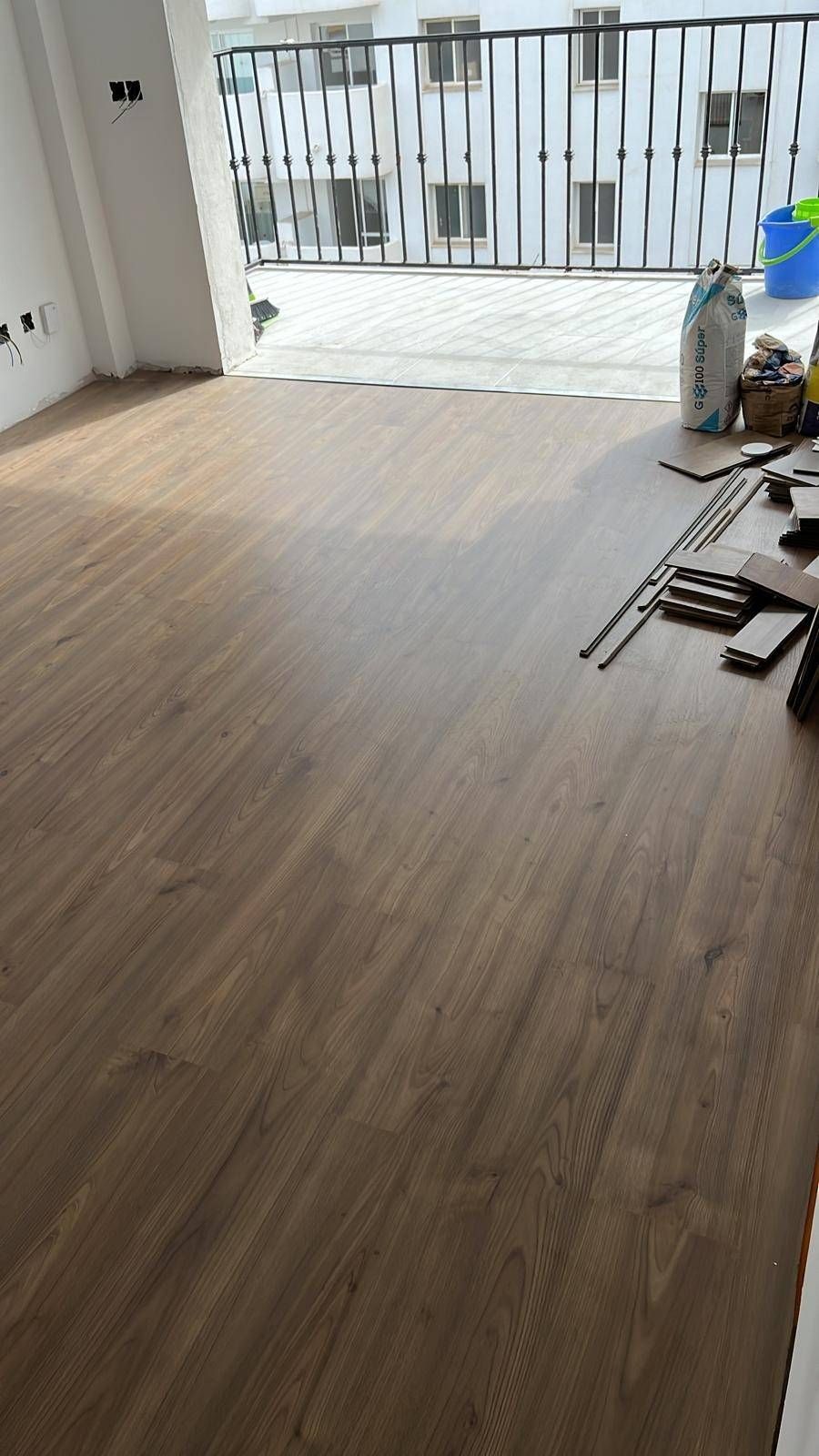Habitación vacía con suelo de madera clara y paredes blancas, con acceso a un balcón con barandilla metálica.