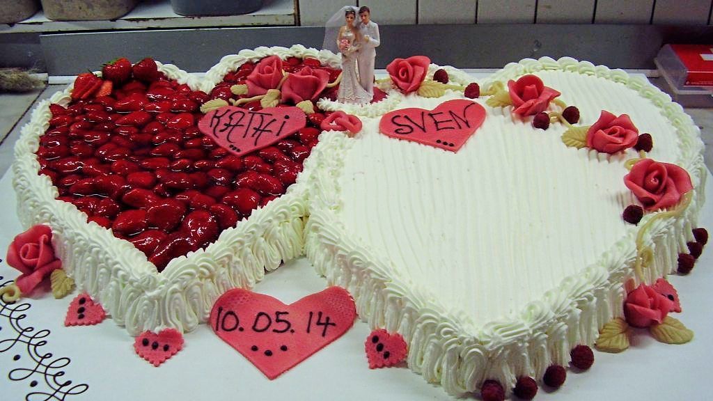herzförmige Hochzeitstorte mit roter Blumendekoration und Hochzeitspaar