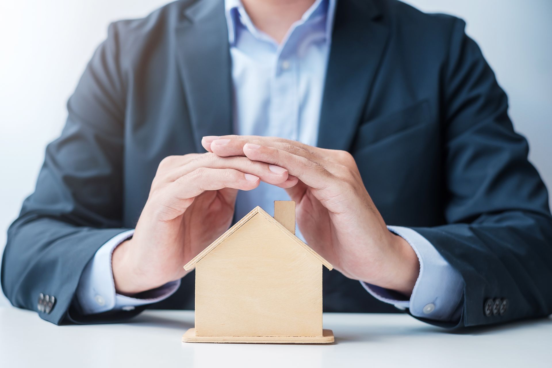 Ein Mann im Anzug sitzt an einem Tisch und hält ein kleines Holzhaus in der Hand.