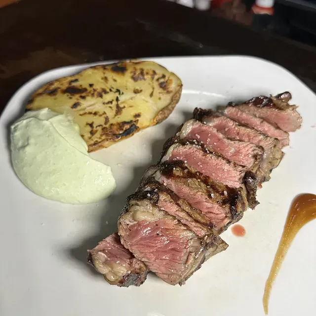 Un plato blanco cubierto con un filete y una patata.