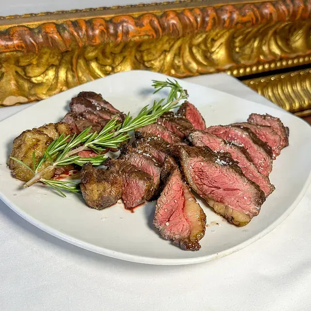 Un plato blanco cubierto con filete en rodajas y verduras.