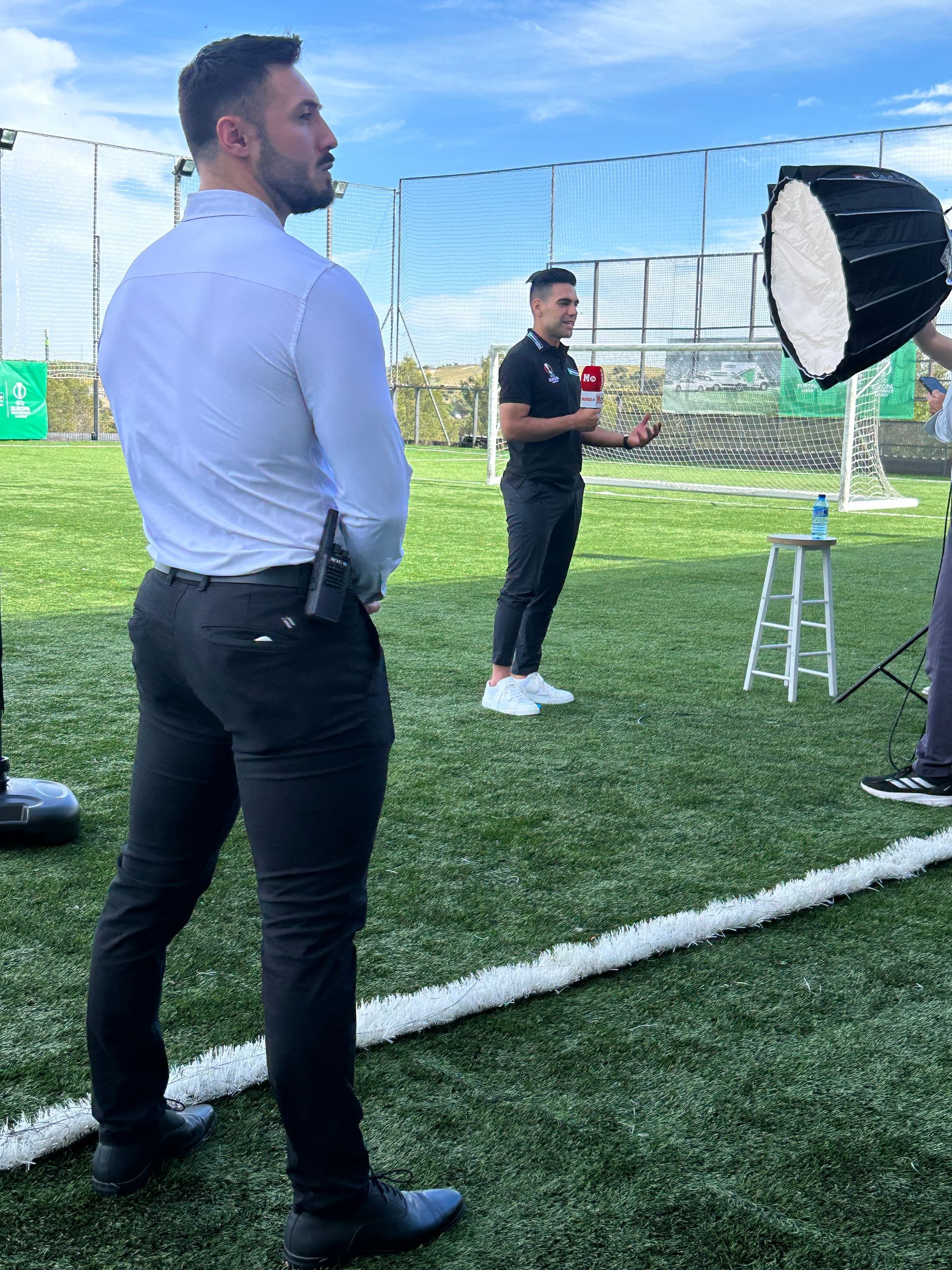 Un hombre con una camisa blanca y pantalones negros está parado en un campo de fútbol.