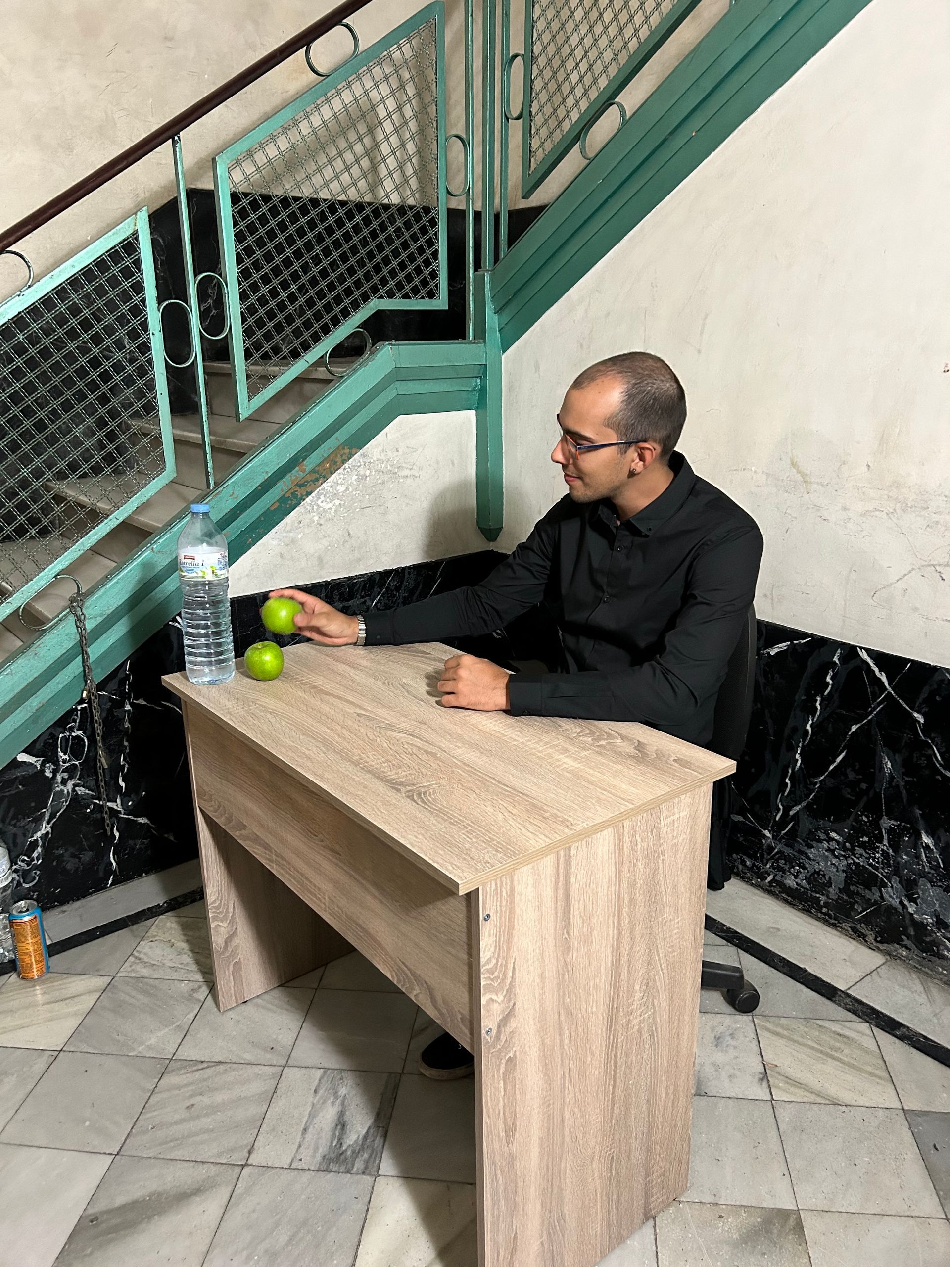 Un hombre está sentado en un escritorio con una manzana y una botella de agua.