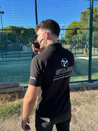 Un hombre está parado frente a una valla hablando por un walkie talkie.