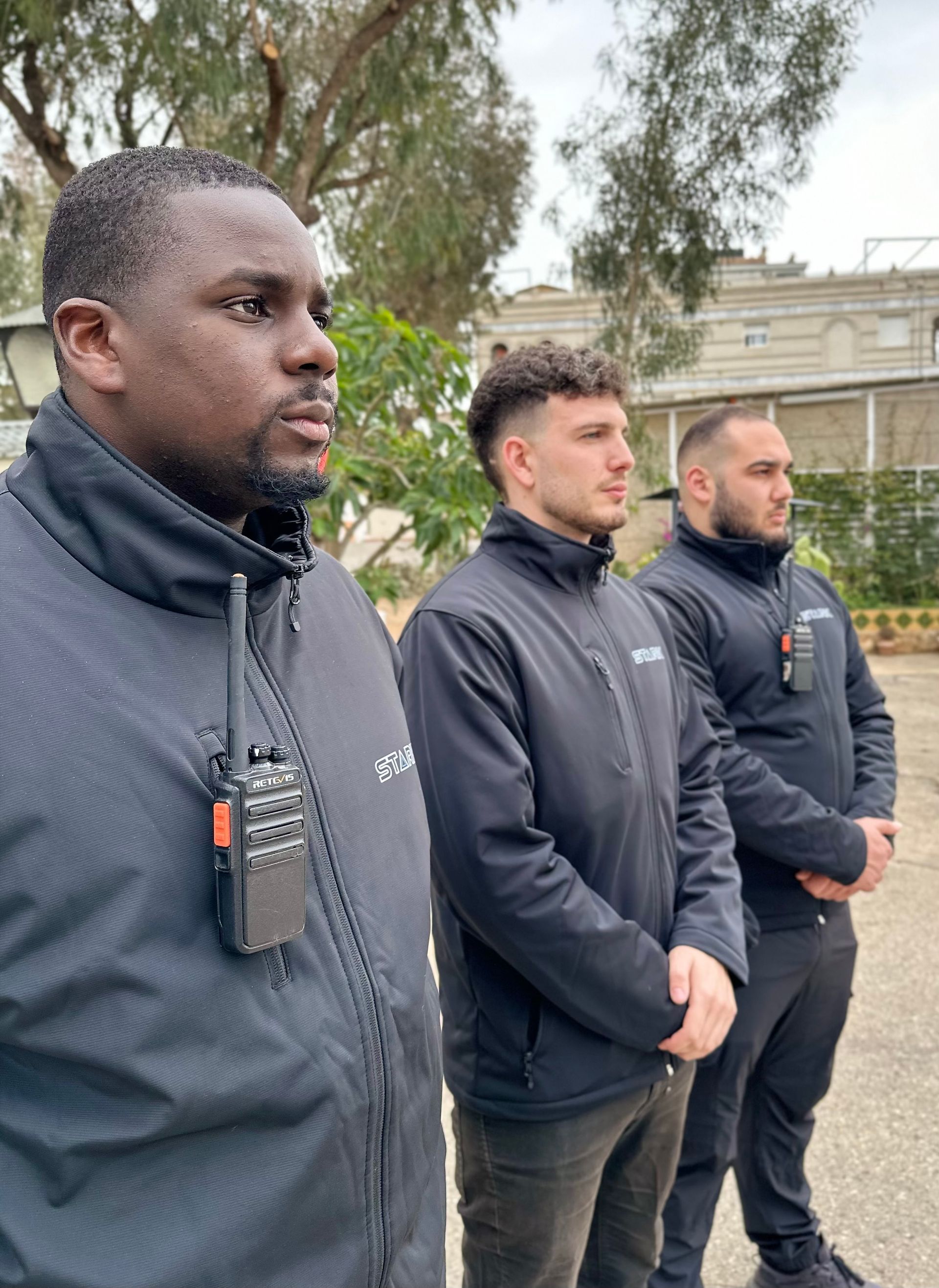 Tres guardias de seguridad están parados uno al lado del otro en un estacionamiento.