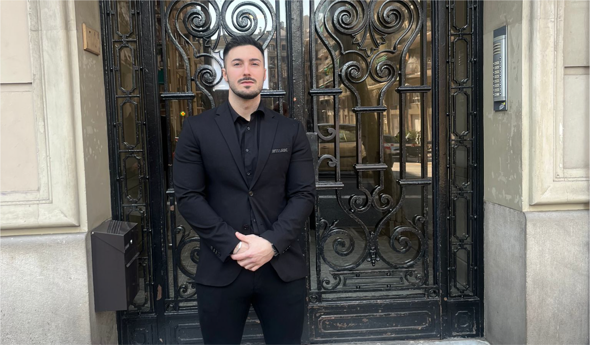 Un hombre con un traje negro está parado frente a una puerta de hierro forjado.
