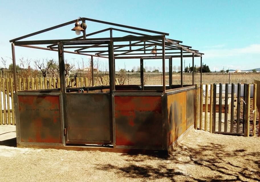 Una estructura de metal se encuentra en el medio de un campo de tierra al lado de una valla de madera.