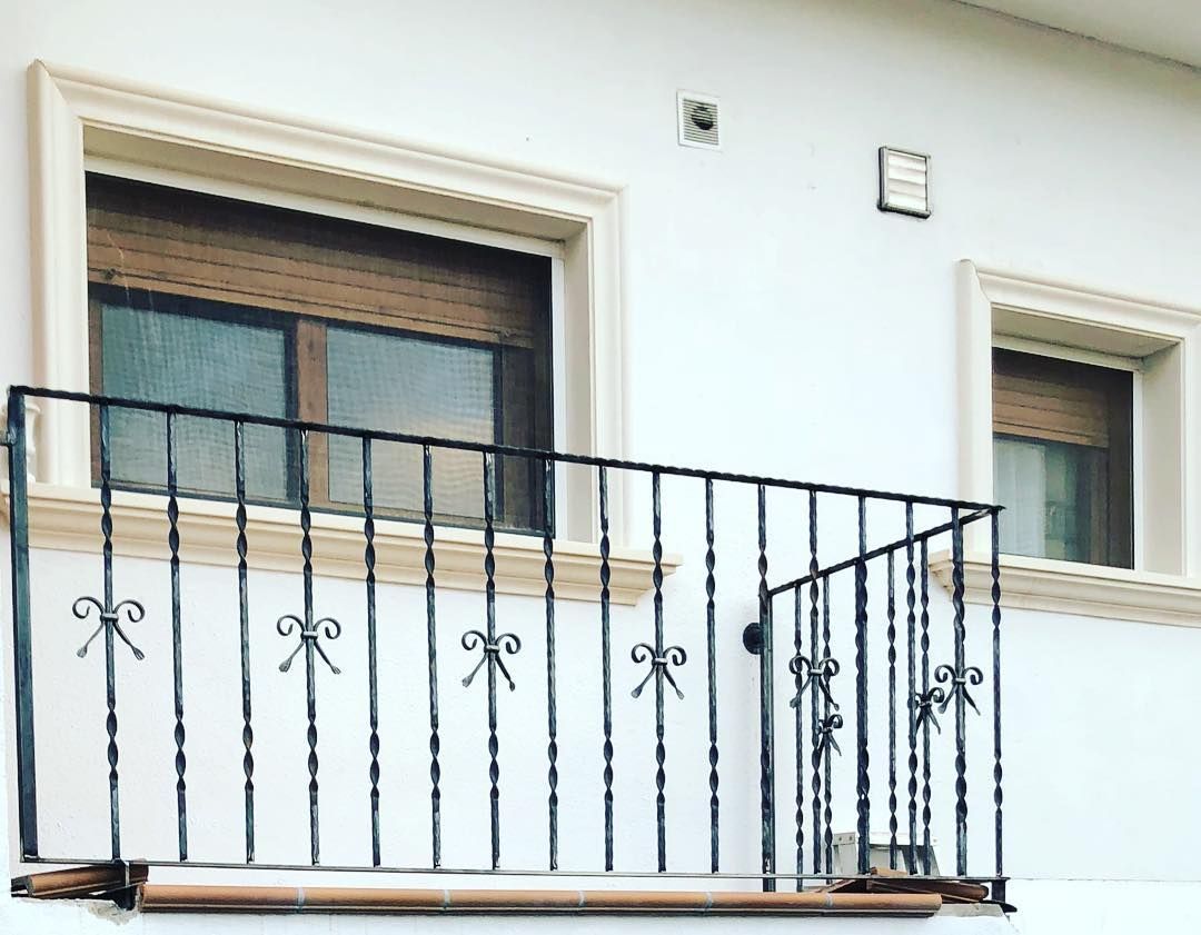 Un balcón con barandilla de hierro forjado y dos ventanas en un edificio blanco.