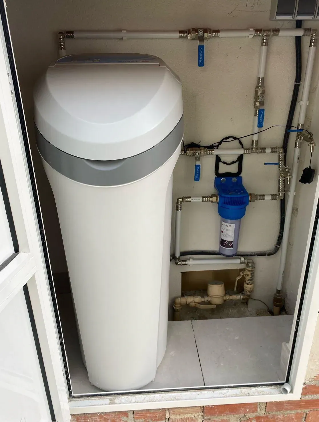 Un descalcificador de agua está en un armario al lado de una ventana.