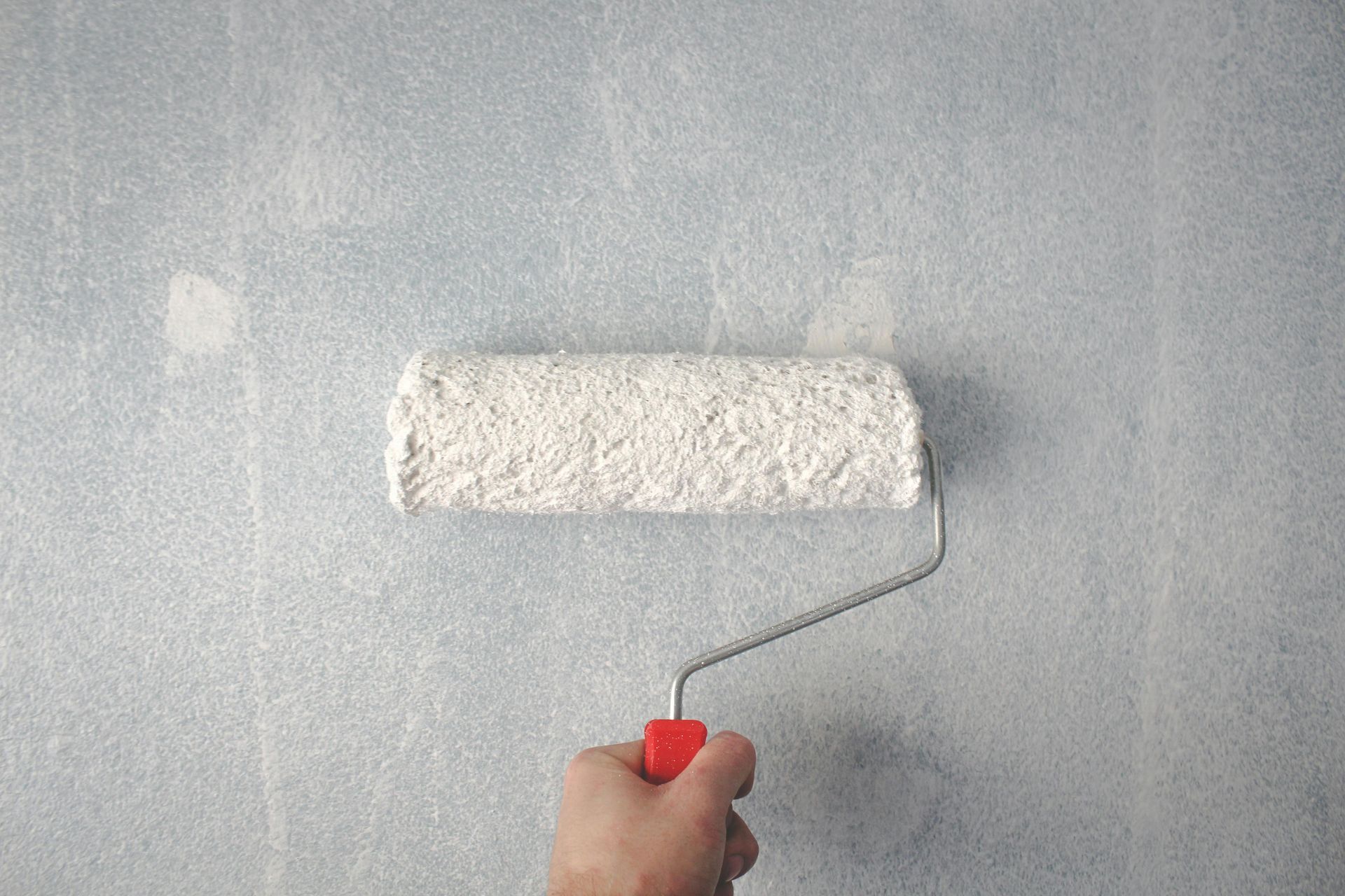 Pintando a mano una pared de color azul pálido con un rodillo de pintura blanco.