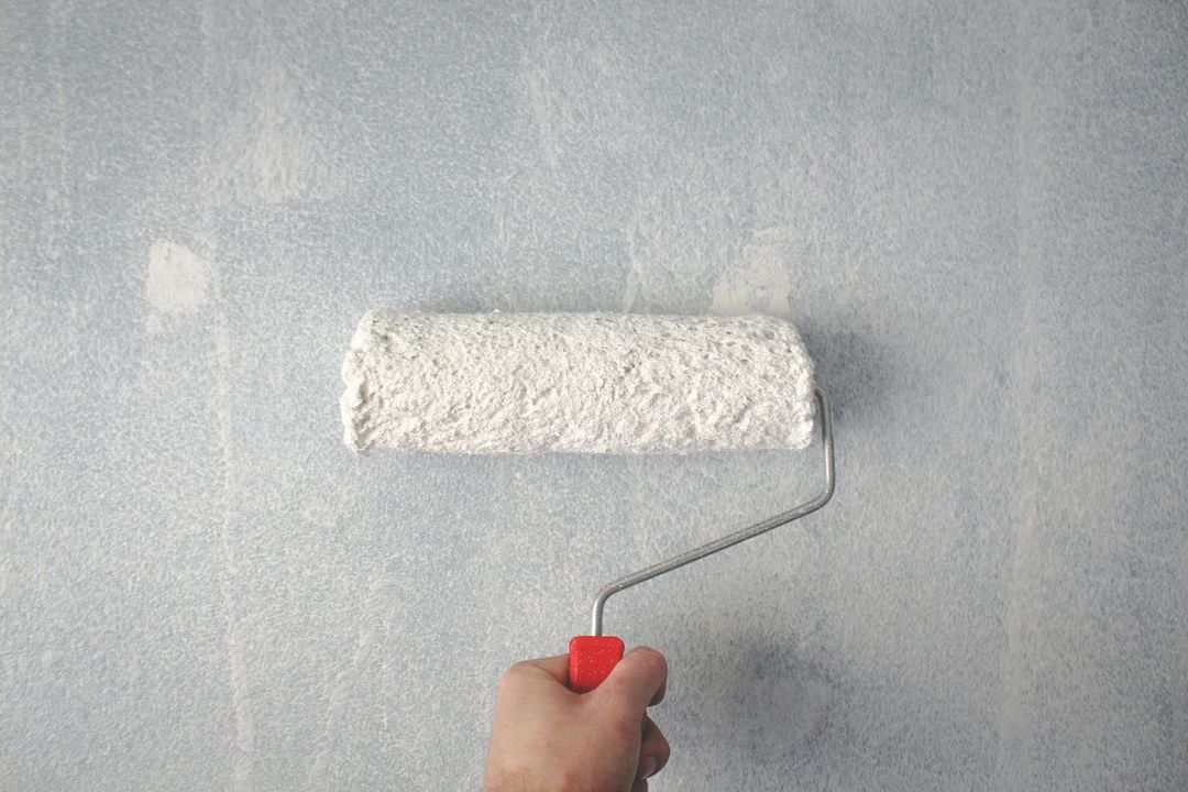 Pintando a mano una pared de color azul pálido con un rodillo de pintura blanco.