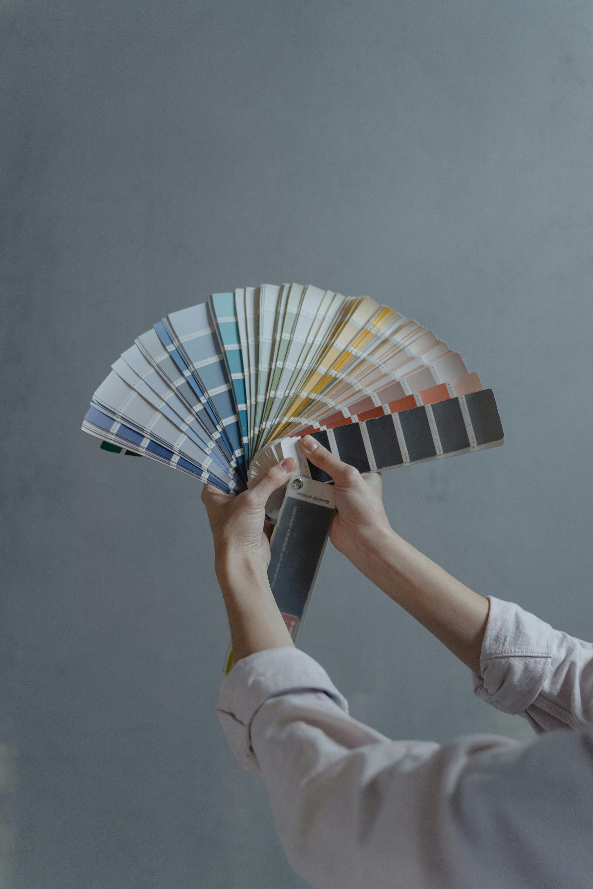 Persona que sostiene una paleta de pintura en abanico con varios tonos, sobre un fondo gris.