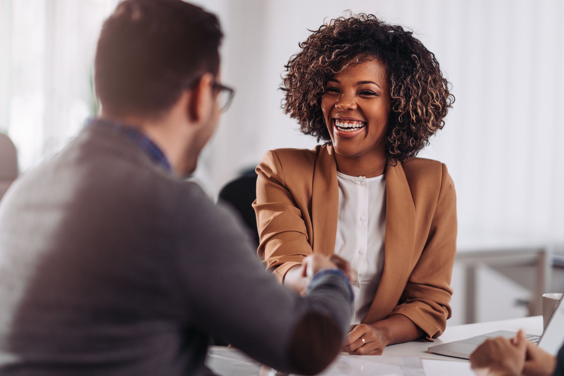 Deux personnes se serrent la main par-dessus une table dans un bureau lumineux, souriant lors d'une réunion.