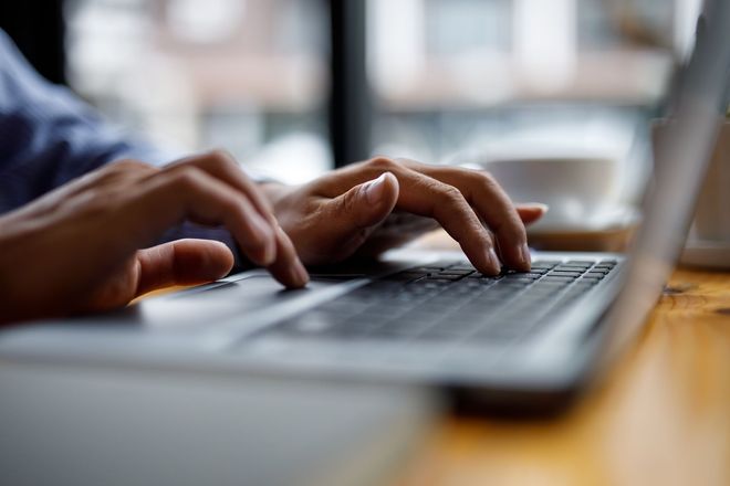 Des mains tapant sur un clavier d'ordinateur portable, en gros plan dans une scène d'intérieur.