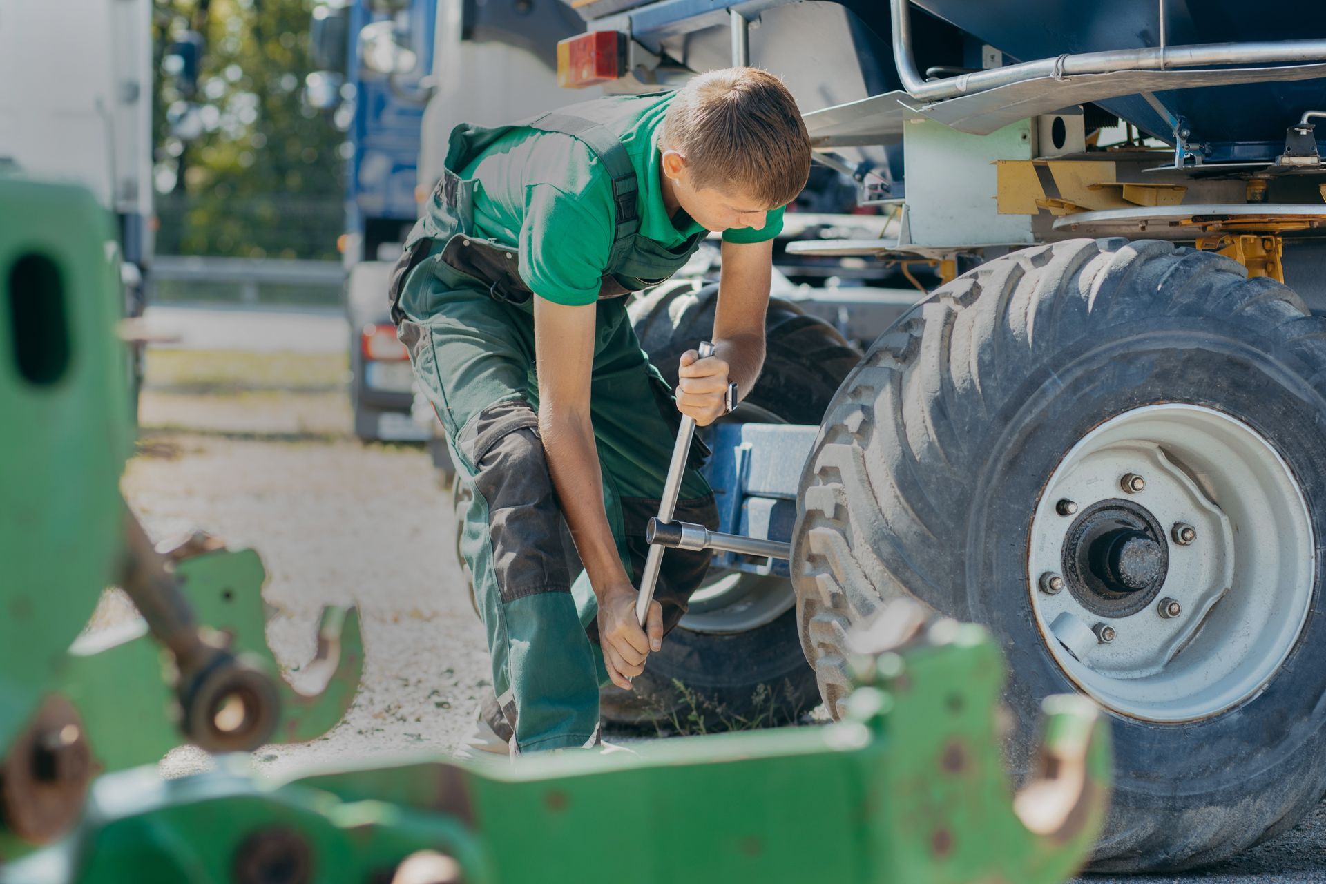 Un mécanicien en chemise verte serre un boulon sur une roue de tracteur à l'extérieur.