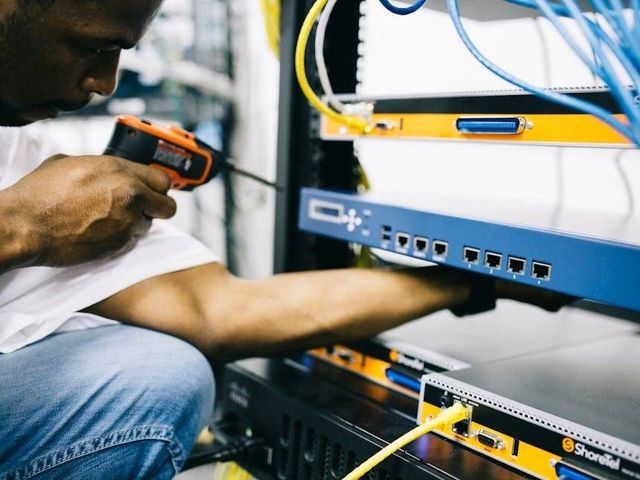 Techniker verwendet einen Barcode-Scanner zur Inspektion von Netzwerkgeräten in einem Serverschrank