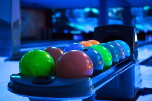 In einer Bowlingbahn stehen auf einem Kugelrücklaufgestell bunte Bowlingkugeln, darunter grüne, rote und blaue.