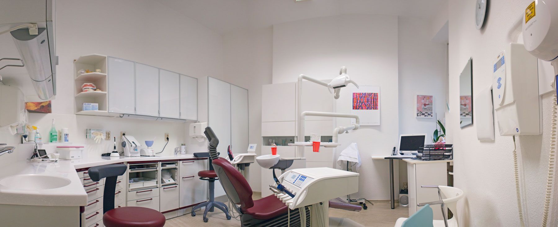 Praxisraum bei Zahnärztin Kristina Latt, mit Liege und Rollhocker, in weiß und burgunder rot