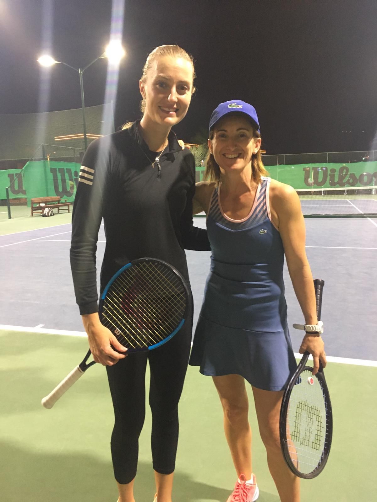 Dos tenistas de pie en una cancha exterior iluminada, con raquetas en mano y sonriendo a la cámara.