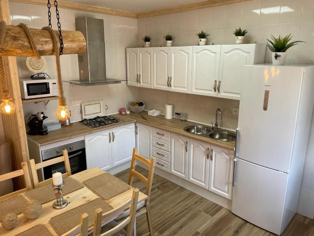 Una cocina con muebles blancos, una mesa y sillas, un refrigerador y un microondas.