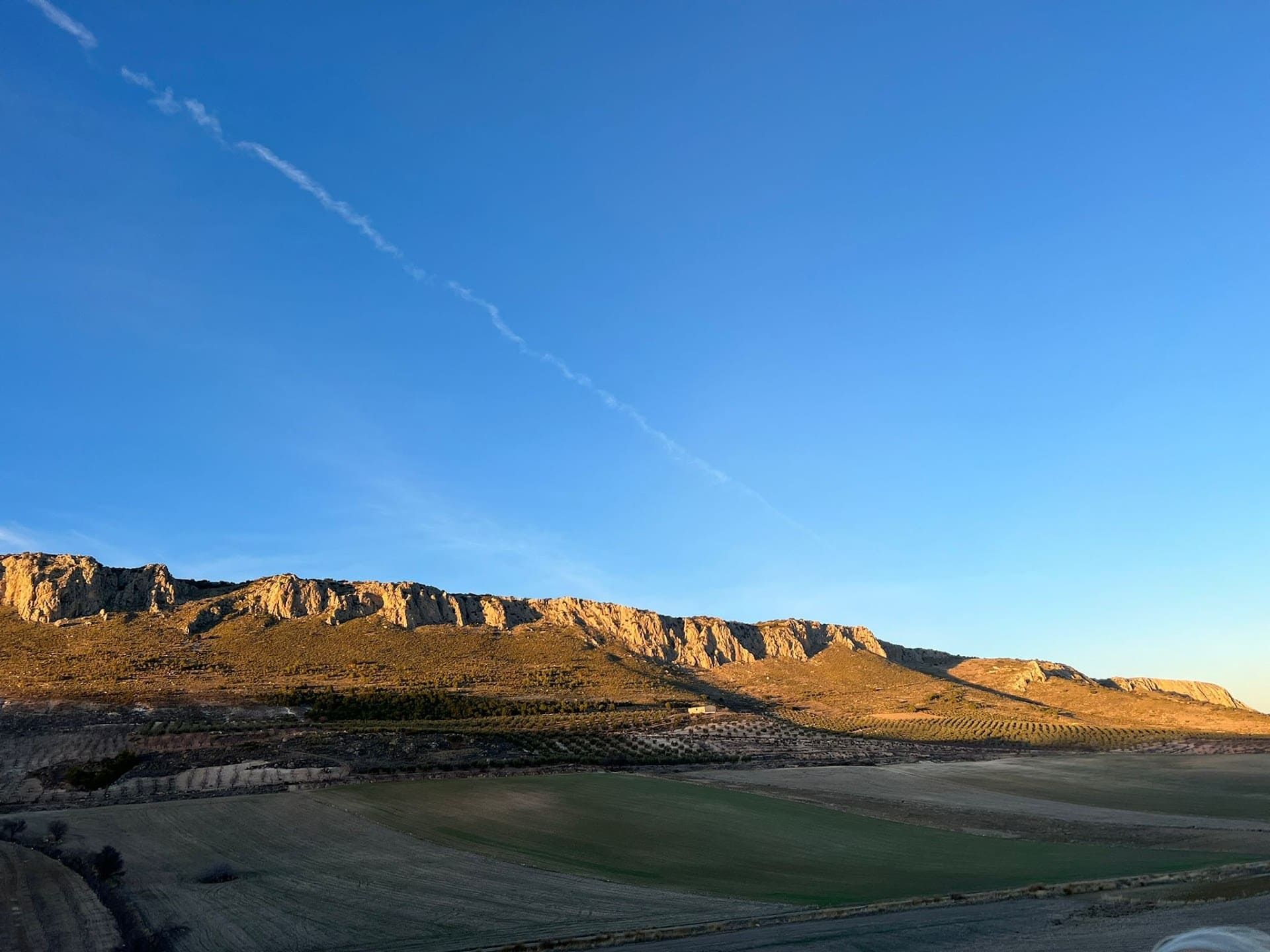 Un paisaje con montañas y un campo en primer plano y un cielo azul en el fondo.