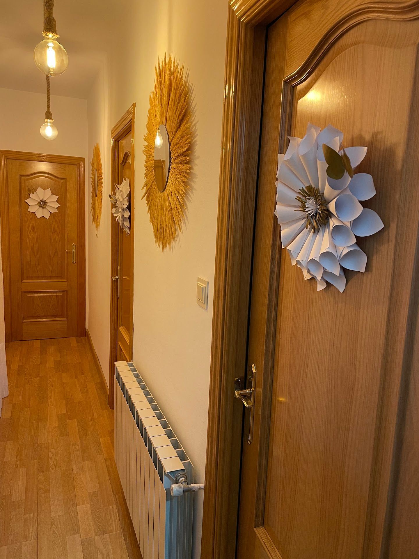 Un pasillo con puertas de madera y un radiador y una corona de flores en la puerta.
