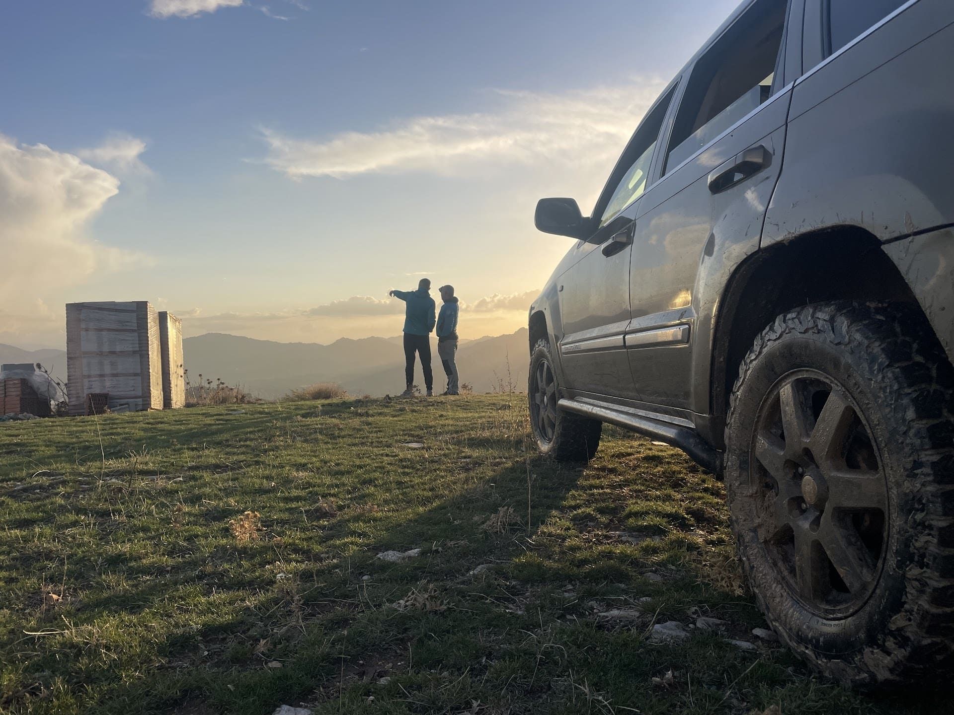 Dos personas están paradas al lado de un automóvil en la cima de una colina cubierta de hierba.