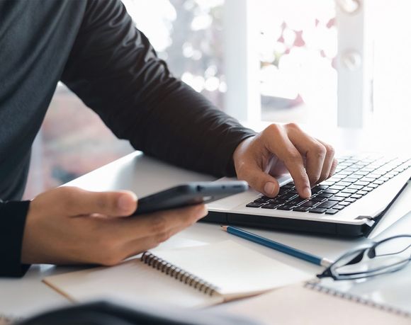 Homme portant une main sur le clavier d'un ordinateur tout en tenant un téléphone cellulaire de l'autre