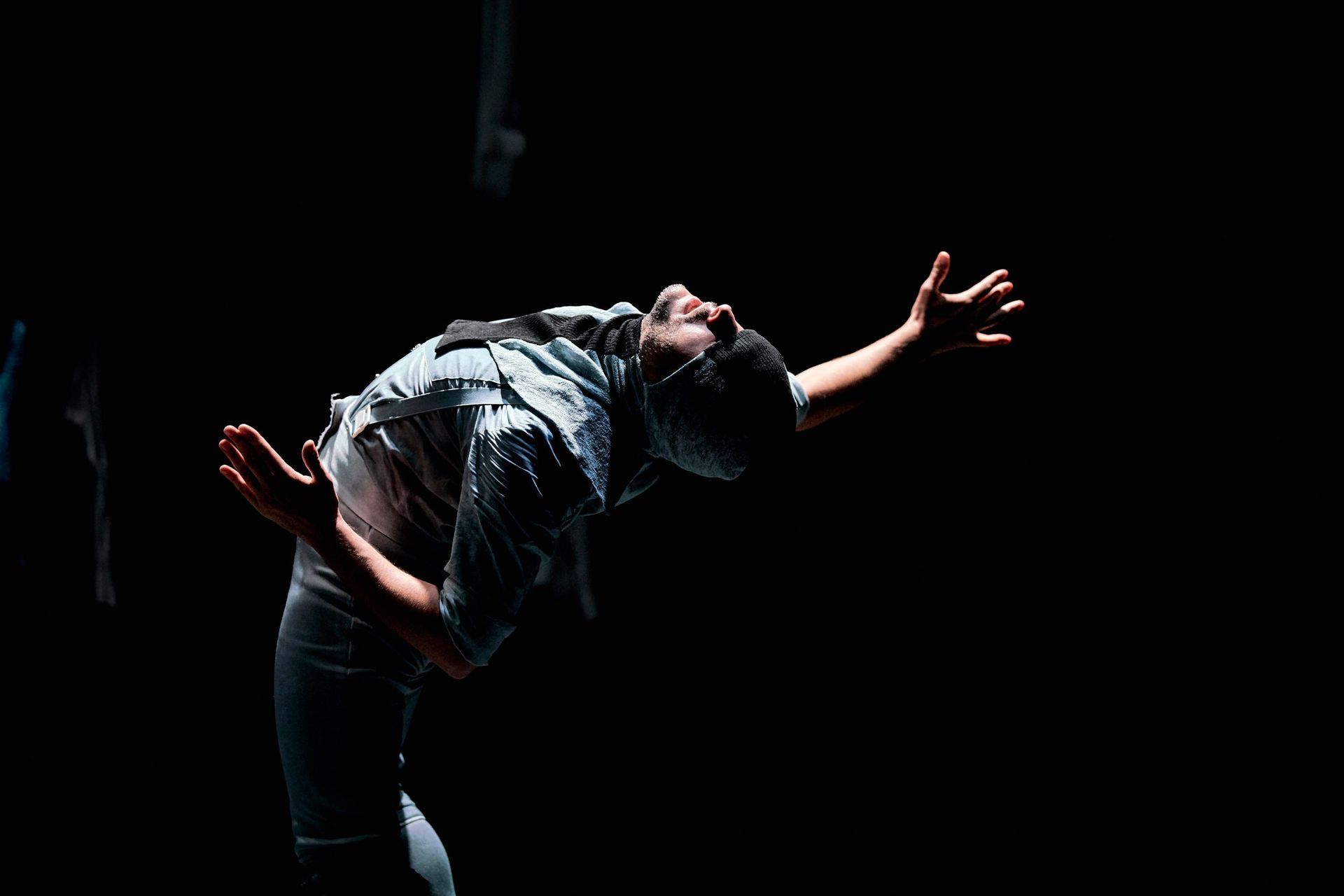 Un hombre baila en la oscuridad con los brazos extendidos.