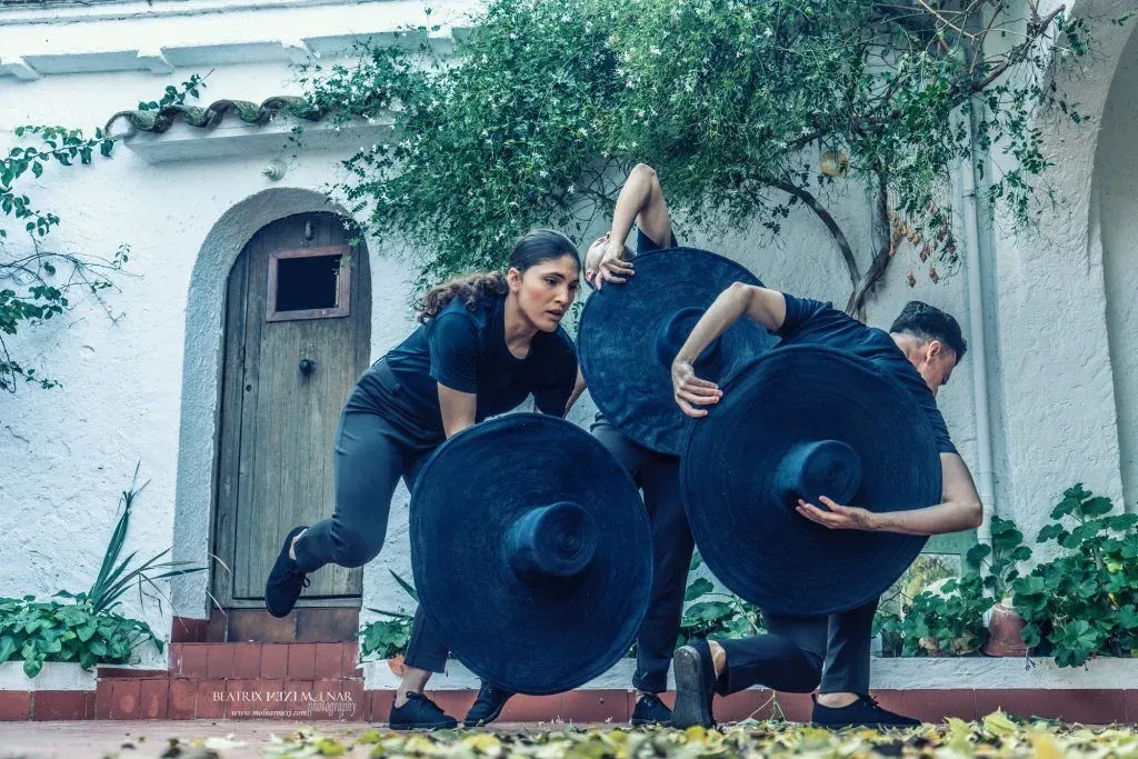 Tres personas con sombreros grandes están paradas frente a un edificio blanco.