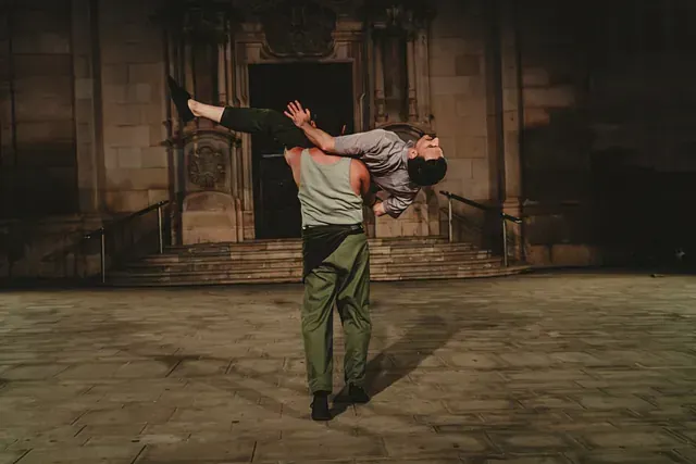 Un hombre sostiene a una mujer en sus brazos frente a un edificio.