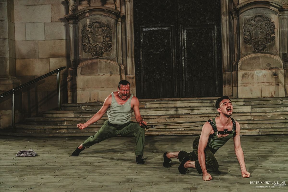 Un hombre con una camisa negra está parado frente a un cartel cultural de 24h la hora.