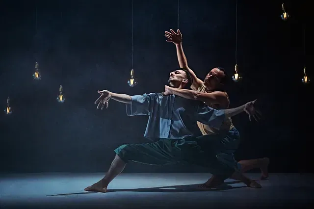 Una pareja de bailarines están bailando en un escenario con luces colgando del techo.