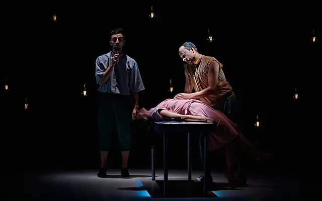 Un hombre está de pie junto a una mujer acostada en una mesa en un escenario.