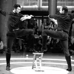 Dos hombres bailan en un taburete delante de una multitud.