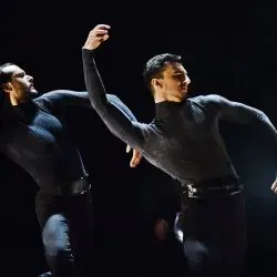 Dos hombres bailan juntos en un escenario en una habitación oscura.