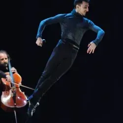 Un hombre está saltando en el aire mientras otro hombre toca un violonchelo.