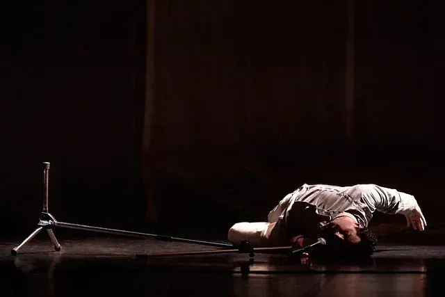 Un hombre está acostado de espaldas en un escenario frente a un micrófono.