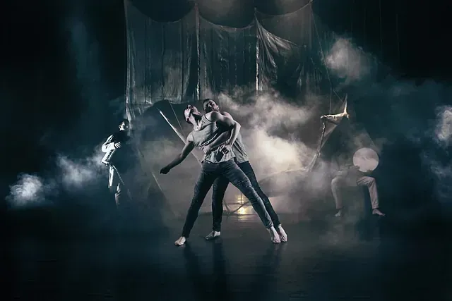 Un grupo de personas está bailando en un escenario en una habitación oscura.