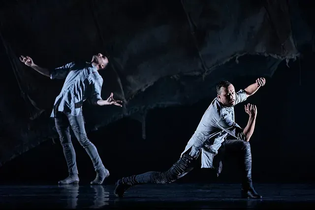 Dos hombres están bailando en un escenario en una habitación oscura.