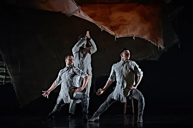 Tres hombres están bailando en un escenario en una habitación oscura.