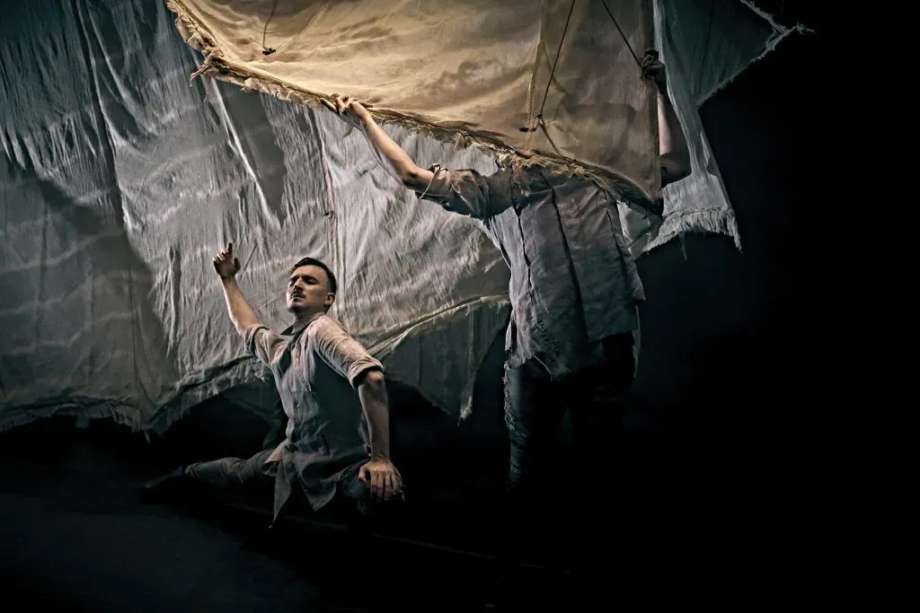 Un hombre está colgado de una gran tela blanca en una habitación oscura.