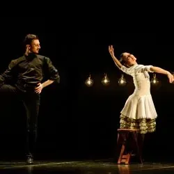 Un hombre y una mujer están bailando en un escenario. La mujer está sentada en un taburete.