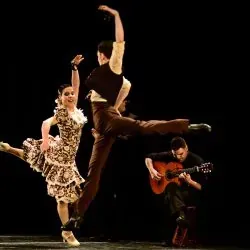 Un hombre toca una guitarra mientras una pareja de bailarines bailan en un escenario.