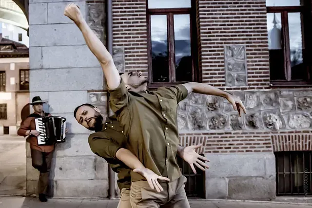 Dos hombres bailan frente a un edificio de ladrillos mientras un hombre toca un acordeón.