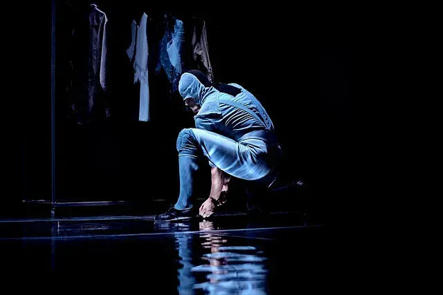 Un hombre con un traje azul está arrodillado en un escenario en la oscuridad.