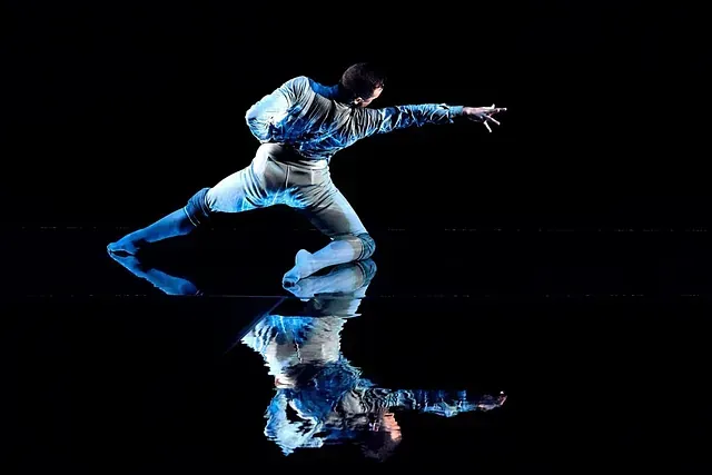 Un hombre está bailando sobre una superficie negra y su reflejo es visible.