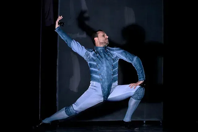Un hombre vestido con un traje azul y blanco está bailando en un escenario.